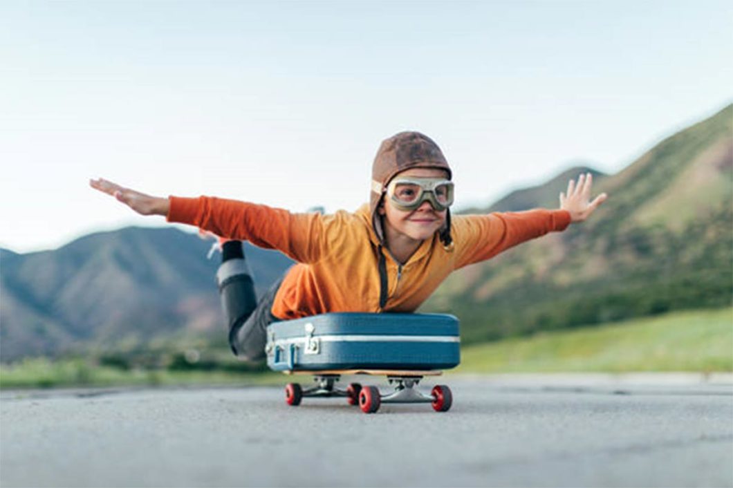 Jeune garçon habillé en aviateur juché sur une valise montée sur une planche à roulettes